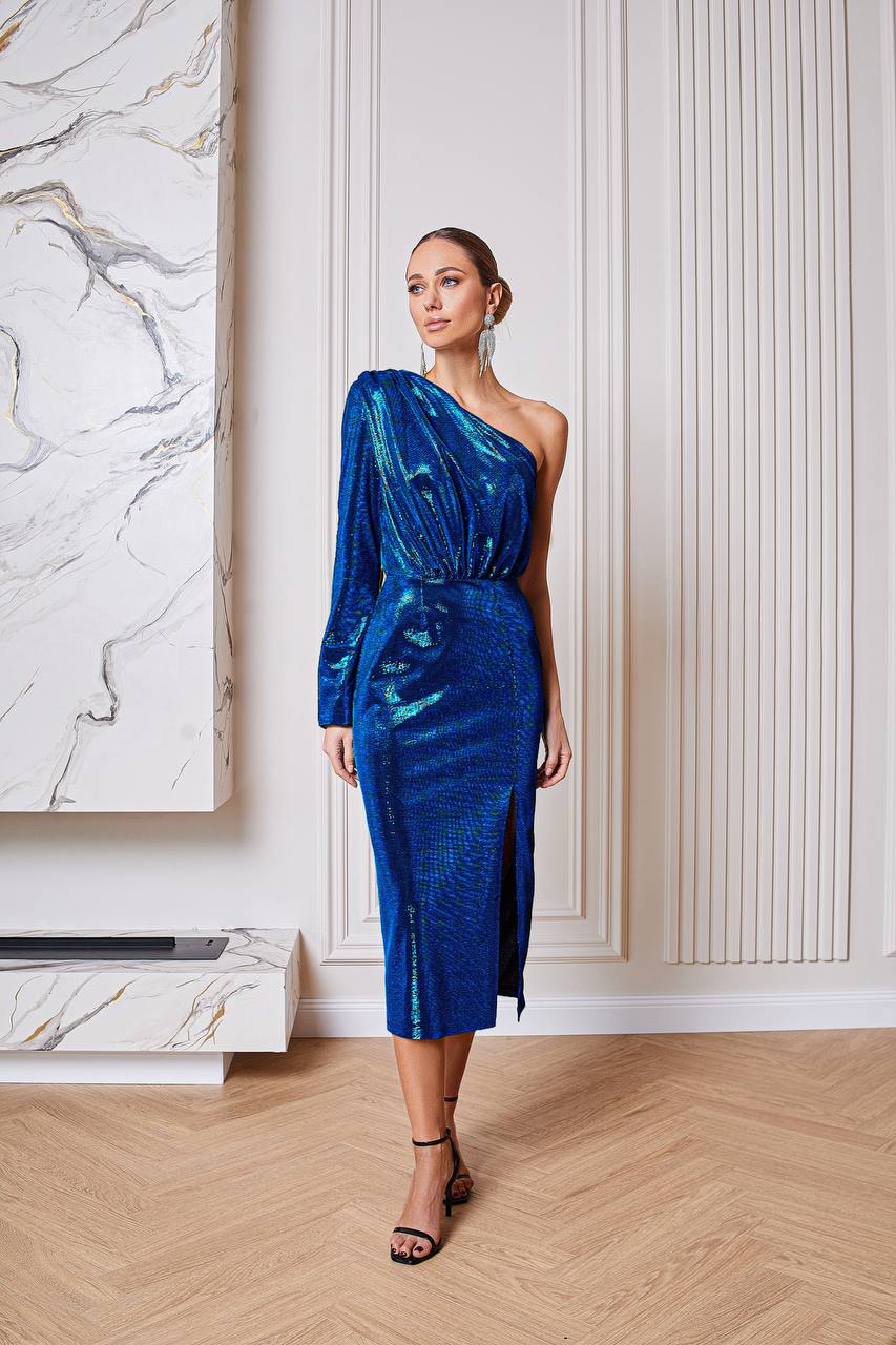 Woman in a blue one-shoulder dress standing in a room with marble wall and wooden floor.