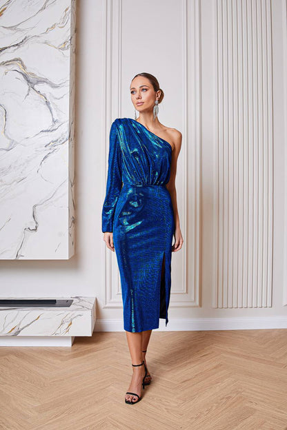 Woman in a blue one-shoulder dress standing in a room with marble wall and wooden floor.