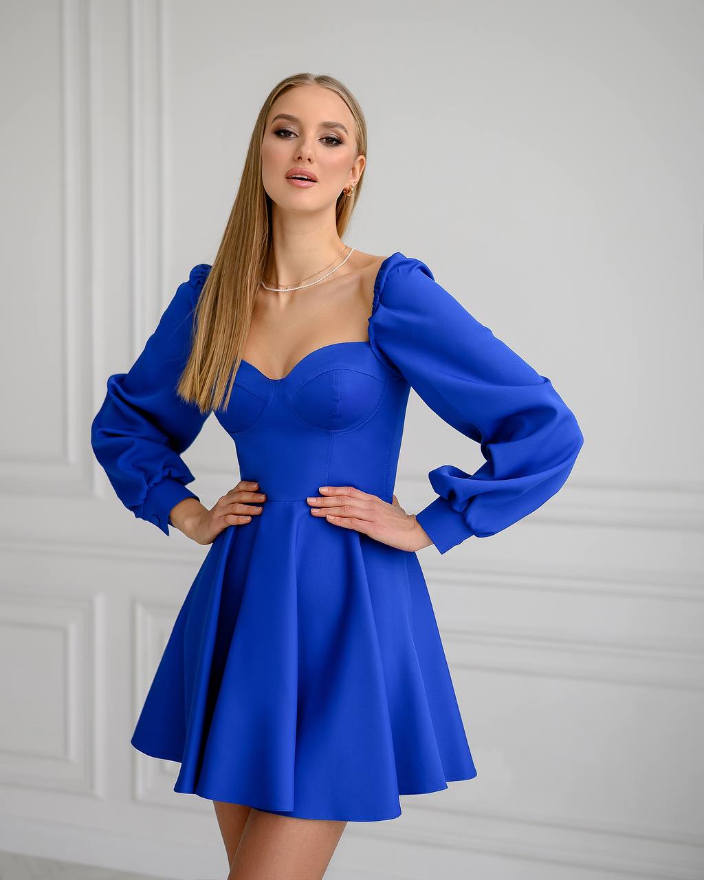 Woman wearing a blue dress with long sleeves against a white wall