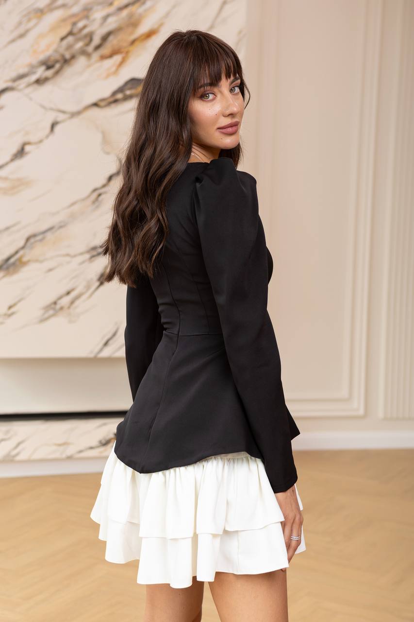 Woman wearing a black blazer over a white dress in an indoor setting