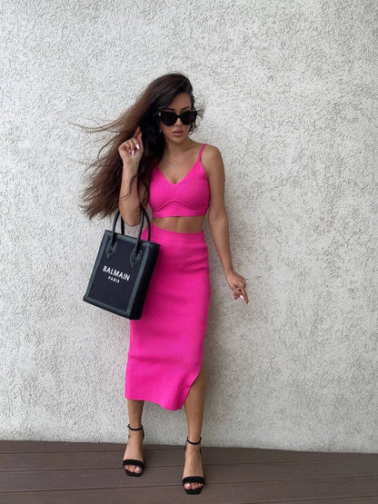 Woman in a bright pink outfit holding a Balmain bag against a textured wall.