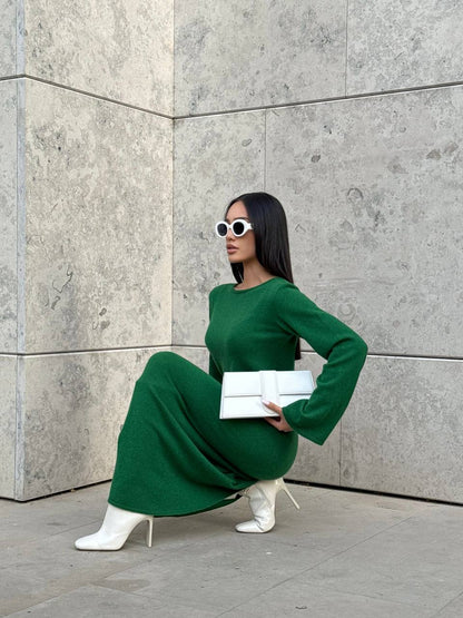 Woman in a green dress posing against a gray wall