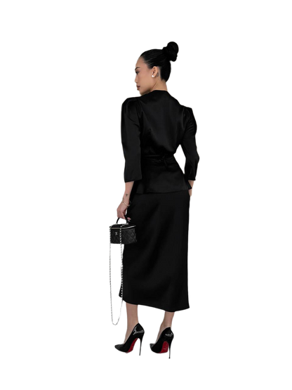 Woman wearing a black outfit with a skirt and top, holding a handbag on a white background