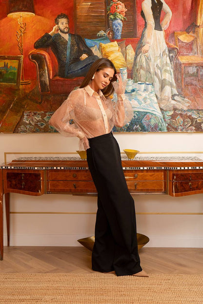 Woman in a stylish outfit standing in a room with classical painting and furniture.