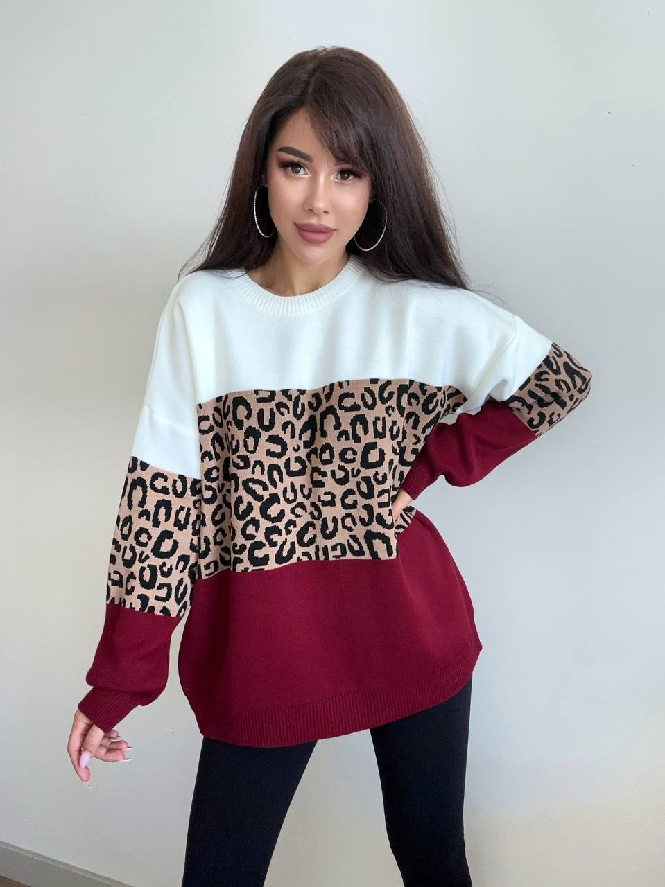 Woman wearing a white and burgundy sweater with leopard print sleeves against a plain background