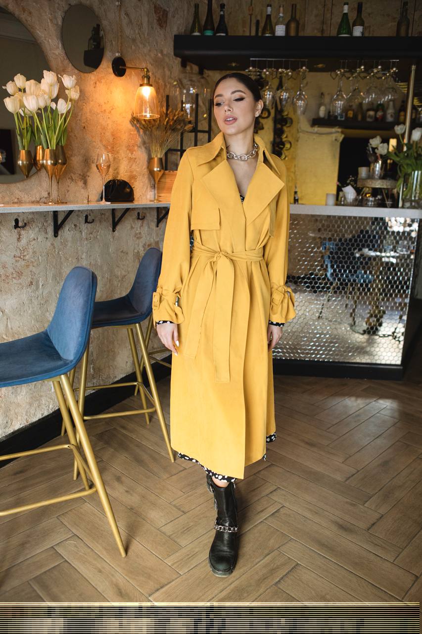 Woman in a yellow trench coat standing in a bar setting