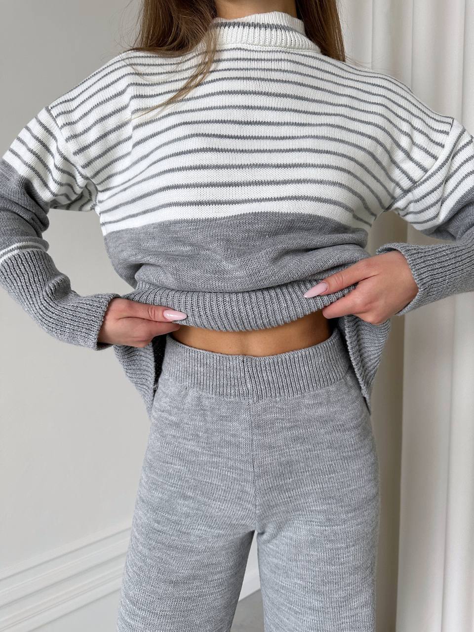 Person wearing a gray and white striped sweater and matching pants against a neutral background
