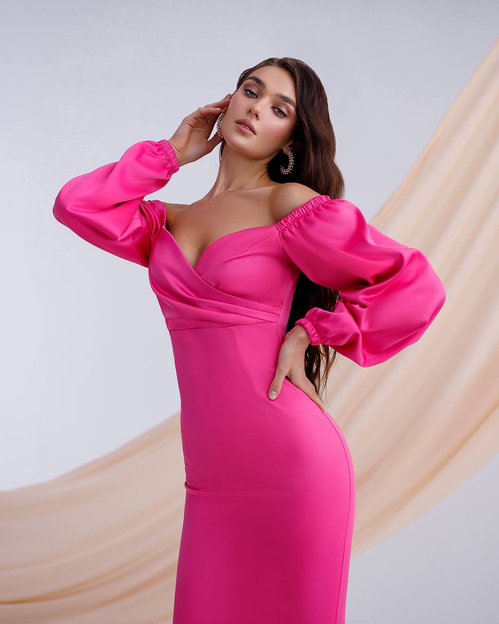 Woman wearing a bright pink off-shoulder dress with puffed sleeves against a neutral background