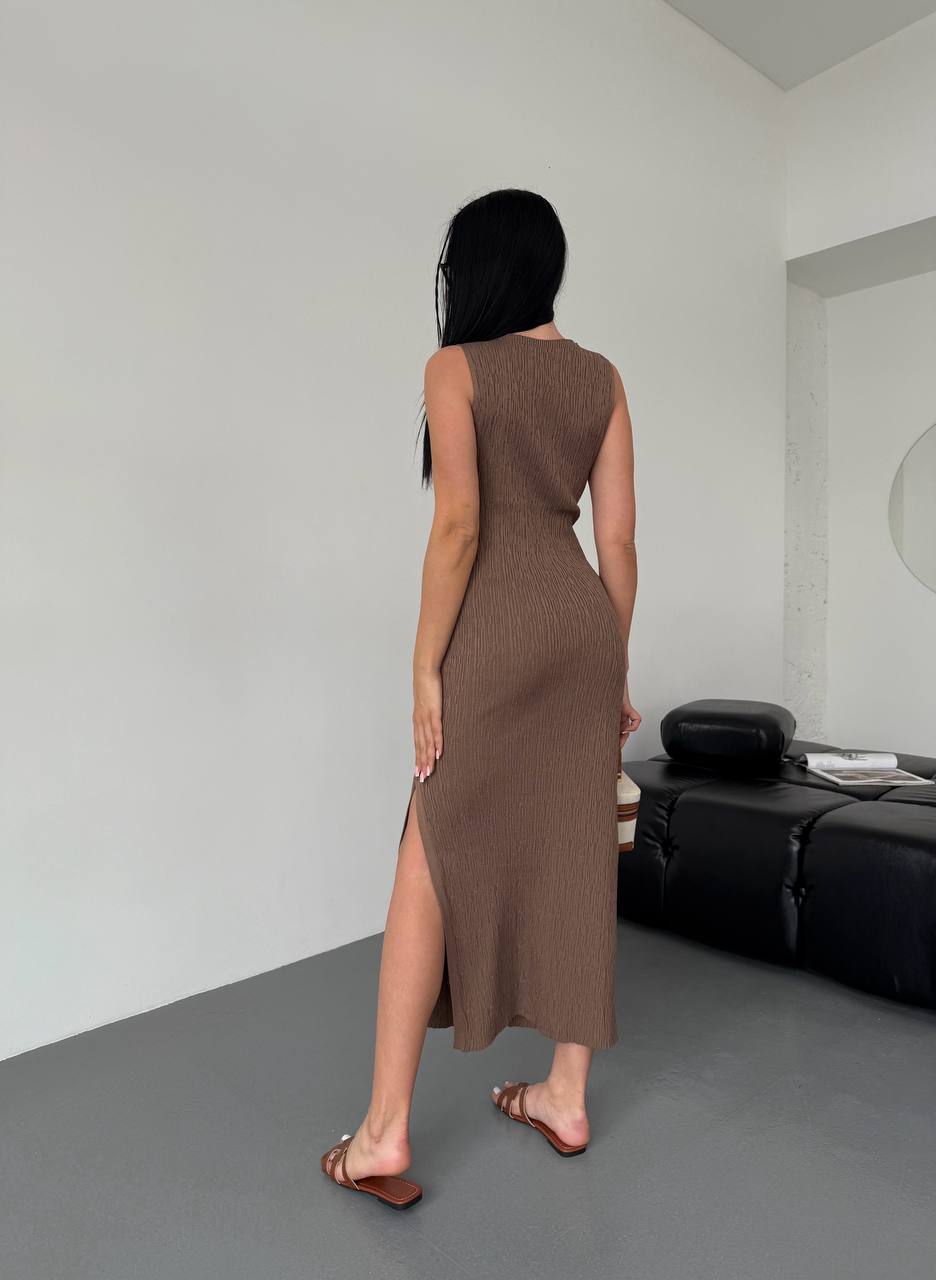 Woman wearing a brown dress standing in a minimalistic room with a white wall and gray floor.