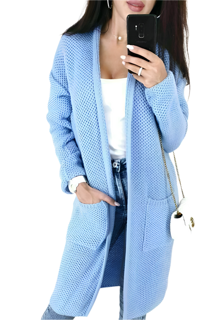 Person wearing a light blue cardigan with a white top and jeans, holding a phone.