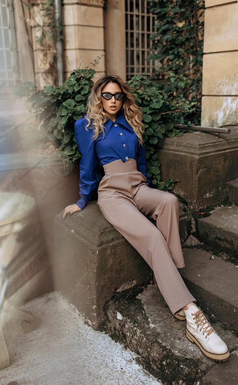 Woman in a blue shirt and beige pants sitting on stone steps with greenery in the background