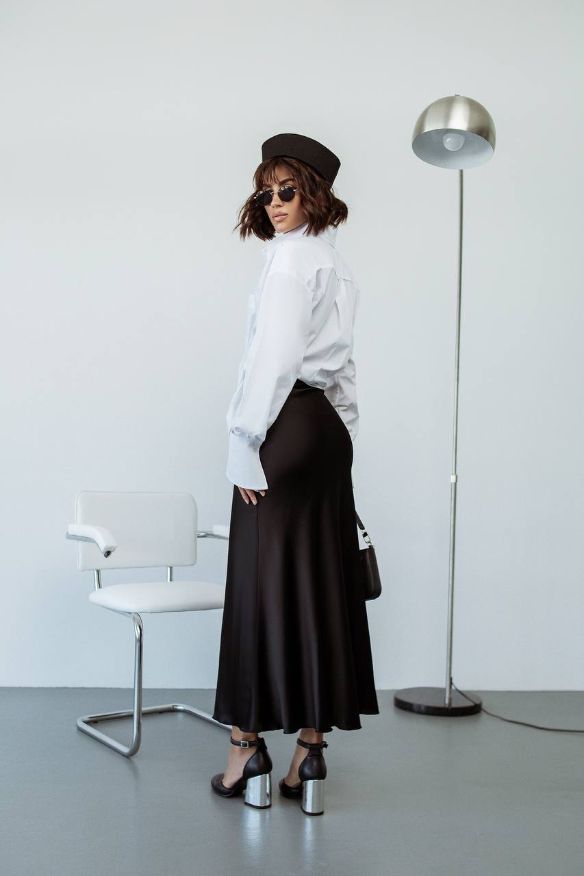 Person wearing a white shirt, black skirt, and hat in a minimalistic room.