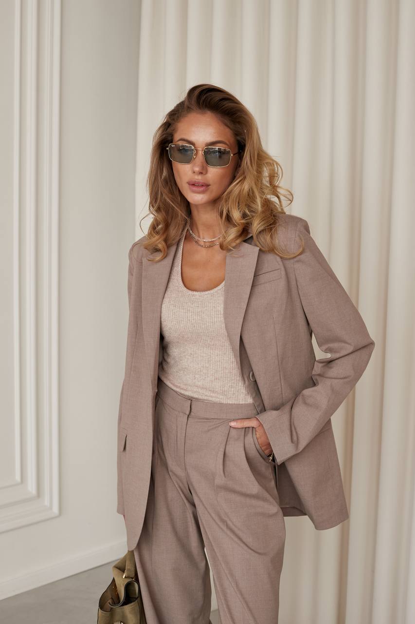 Woman wearing a beige suit with sunglasses against a neutral background