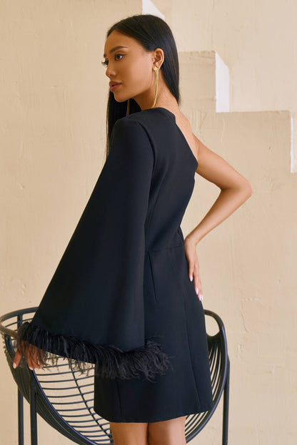 Woman wearing a black dress with ruffled sleeves against a beige wall.