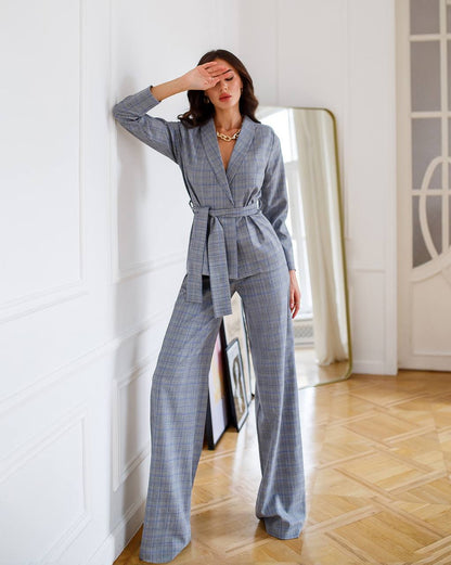 Woman in a gray checkered outfit standing in a room with a mirror and light-colored walls.