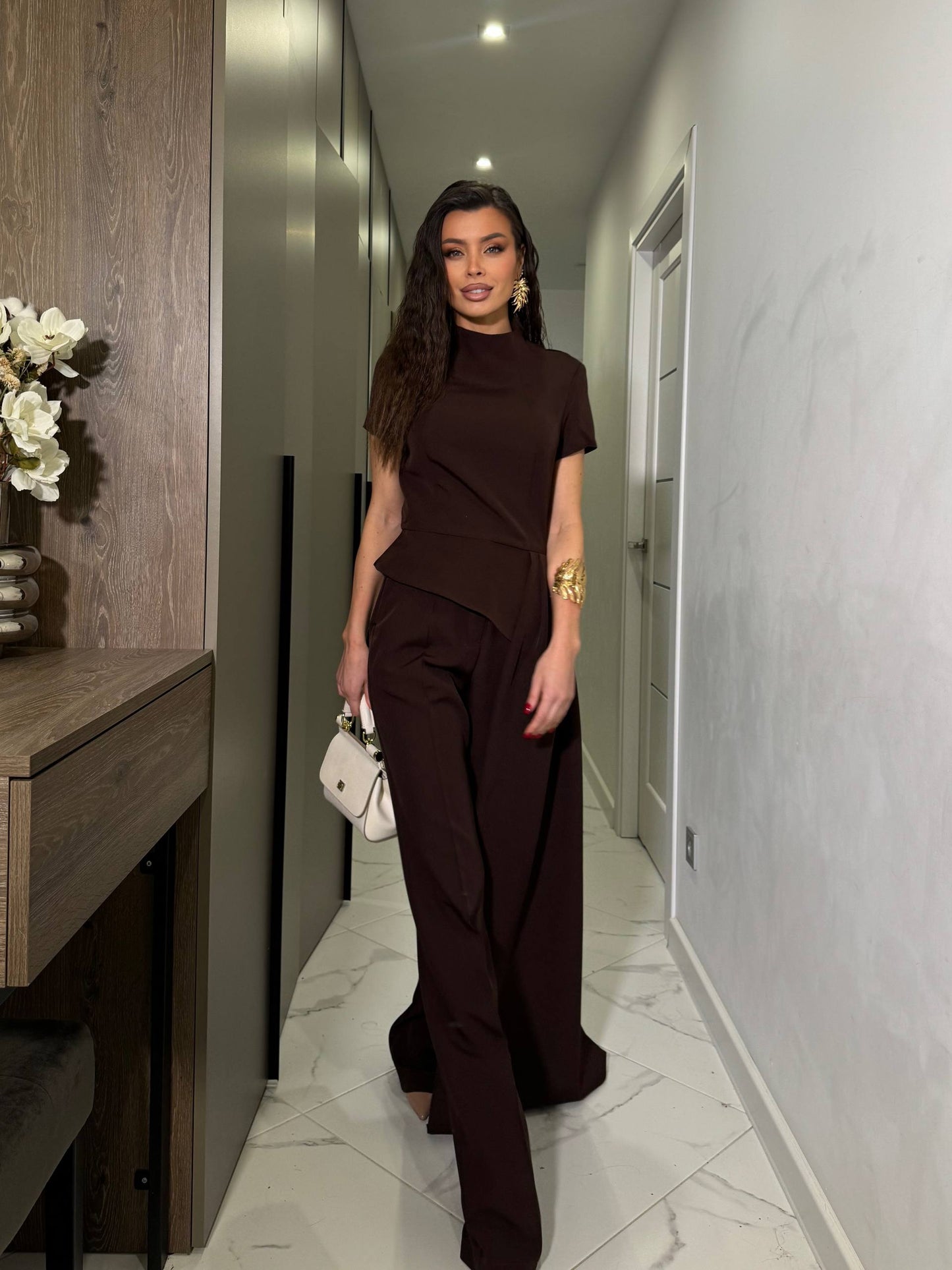 Woman in a brown outfit standing in a modern hallway.