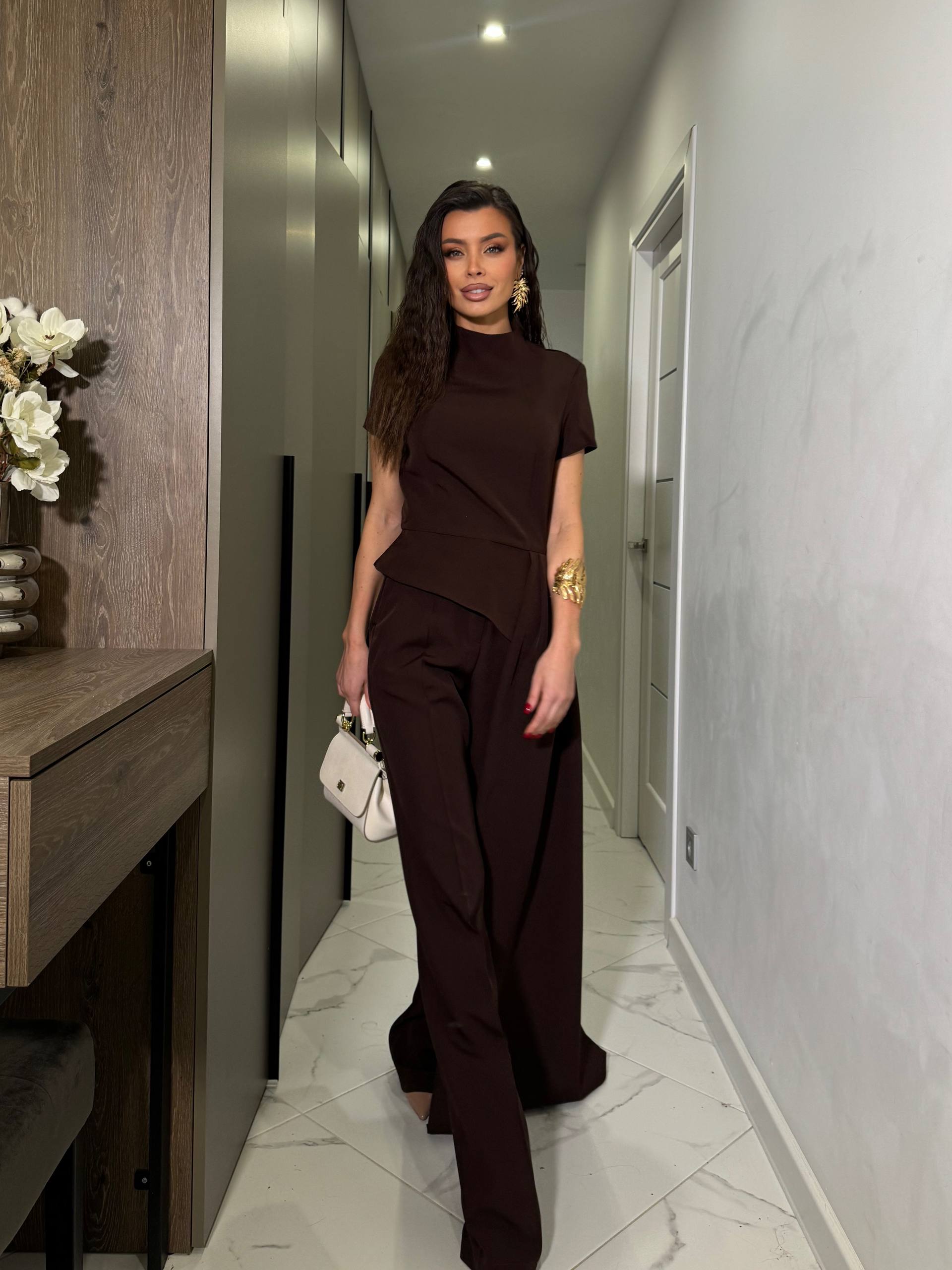 Woman in a brown outfit standing in a modern hallway.