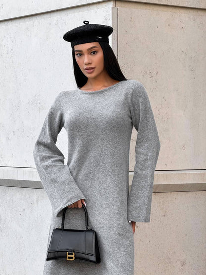 Woman wearing a gray sweater dress and black beret against a light-colored wall.