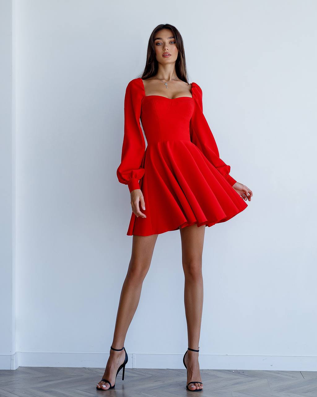 Woman wearing a red dress with long sleeves against a white wall
