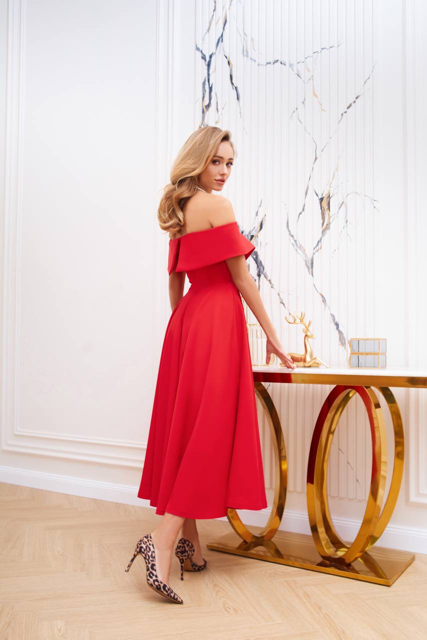 Woman in a red off-shoulder dress standing in a stylish interior setting.