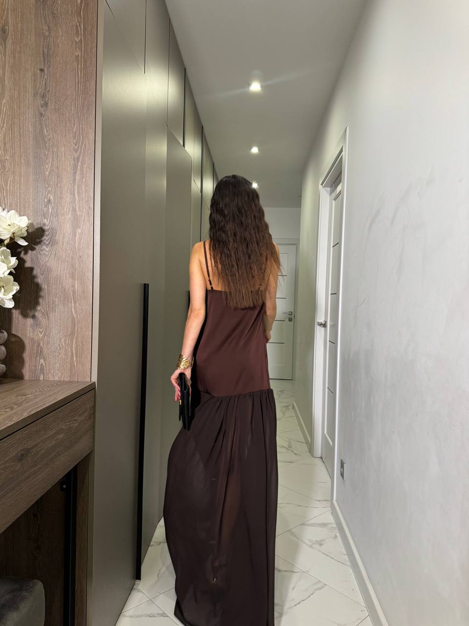 Woman in a brown dress walking down a hallway in a modern home.