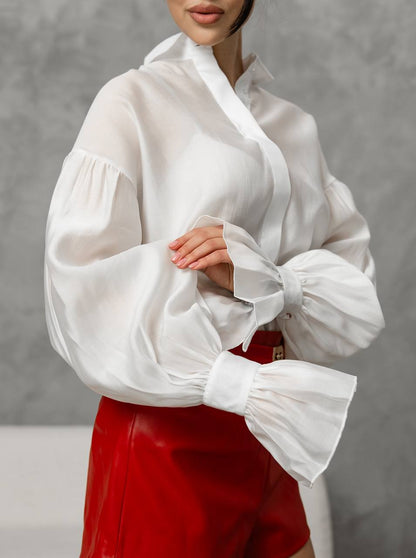 White blouse with puffed sleeves worn by a person against a gray background