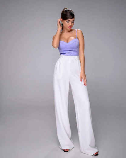 Woman wearing a purple top and white pants against a gray background