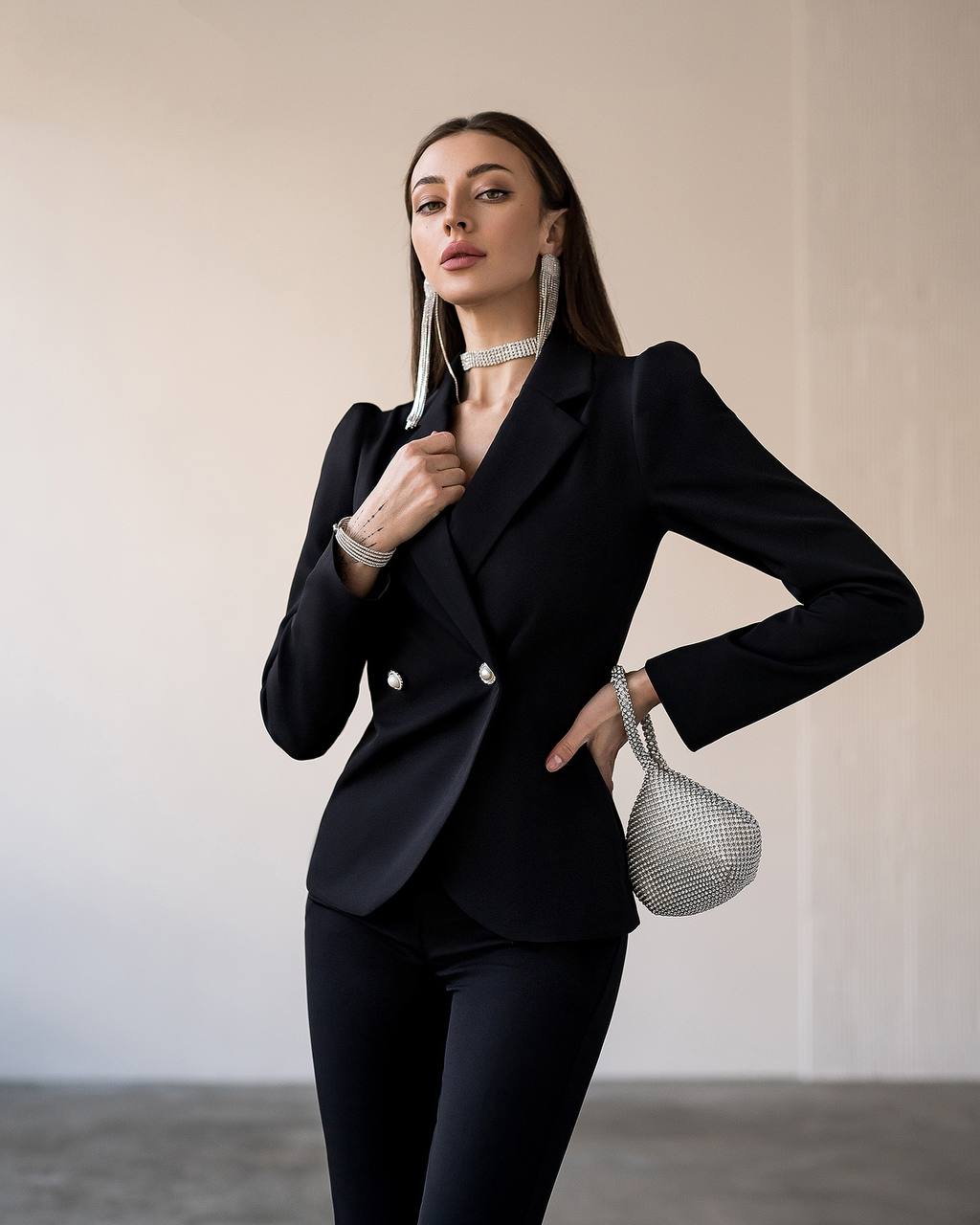 Woman in a black suit holding a silver handbag against a neutral background