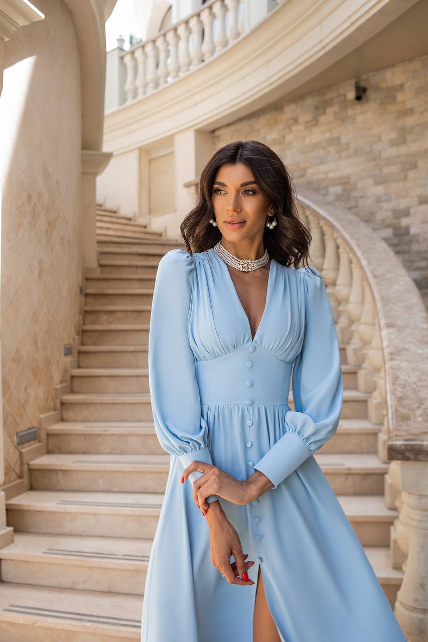 Woman in a light blue dress standing on a staircase with classical architecture.