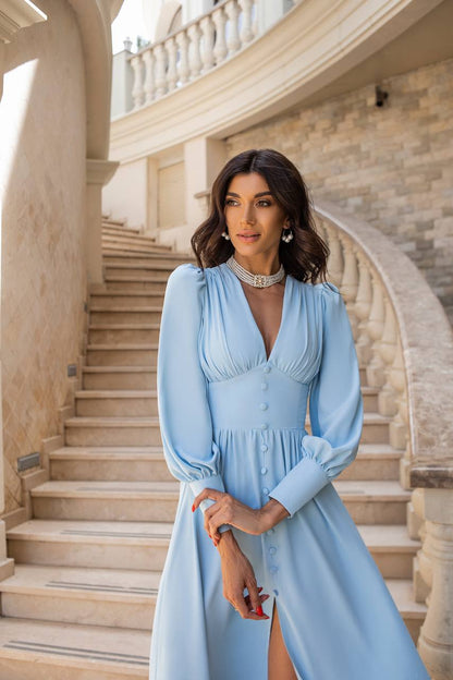 Woman in a light blue dress standing on a staircase with classical architecture.