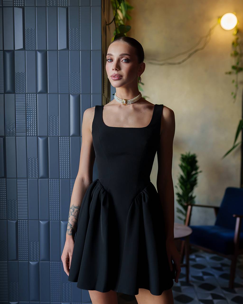 Woman wearing a black dress standing against a textured blue wall.