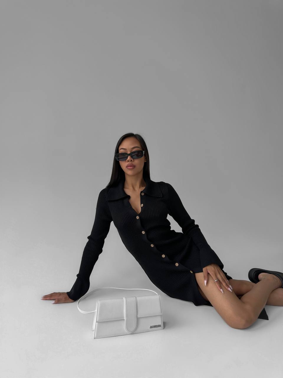 Woman in a black outfit sitting on a white surface with a gray background