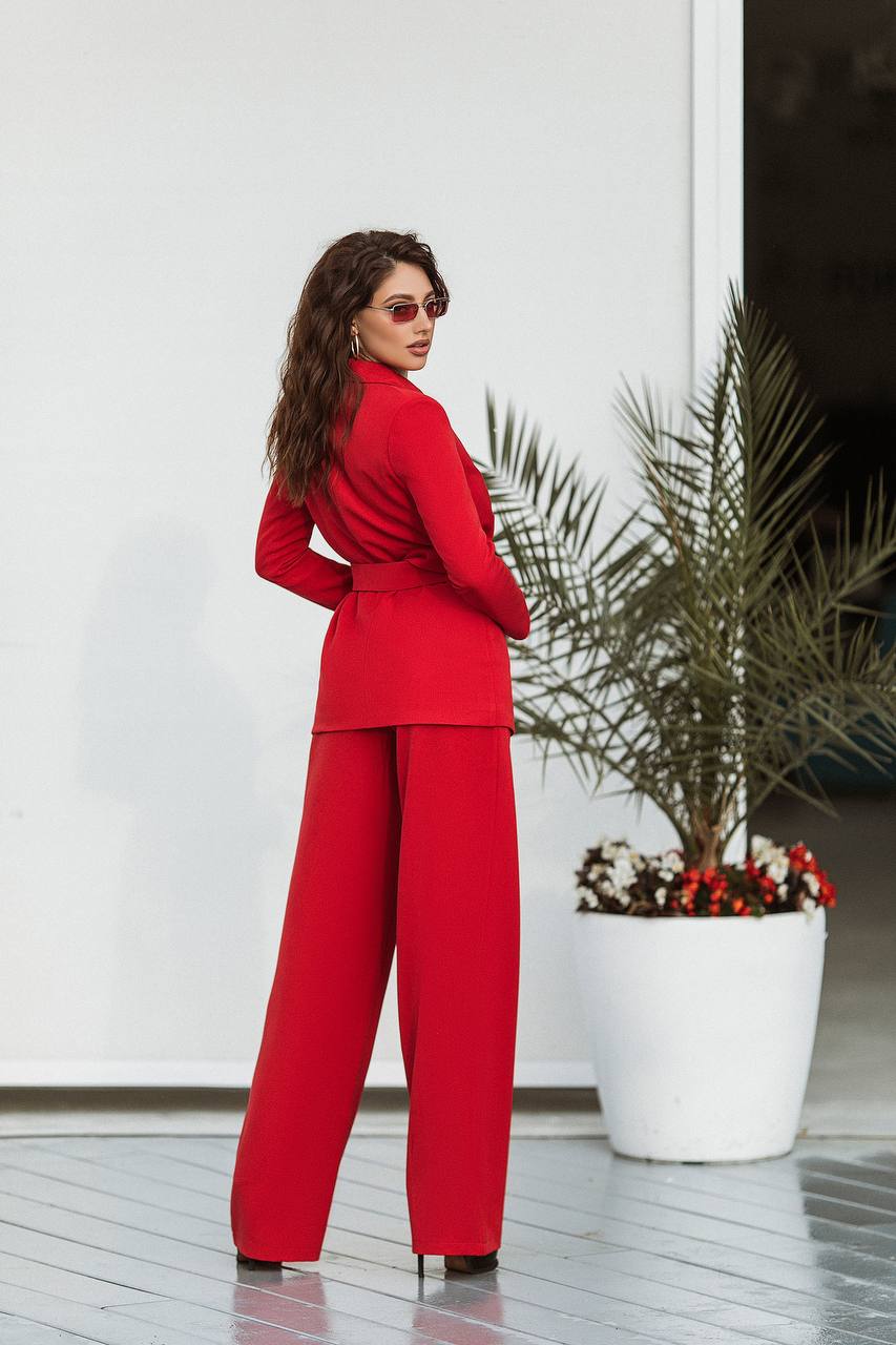 Woman in a red outfit standing in front of a white wall with a plant.
