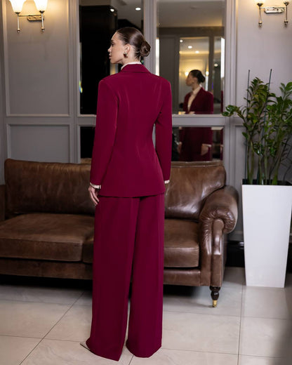 Woman in a burgundy suit standing in a room with a brown leather couch and a plant.