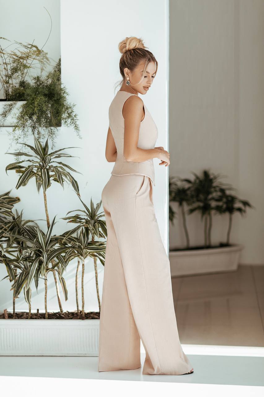 Woman in a beige jumpsuit standing in a room with plants