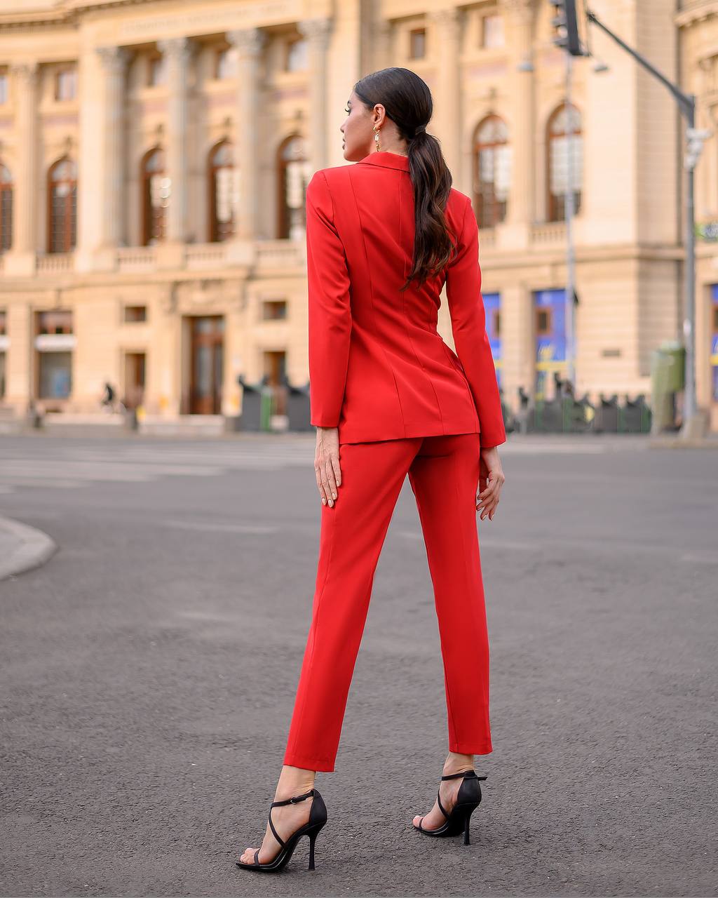 Woman in a red suit standing on a street with a building in the background