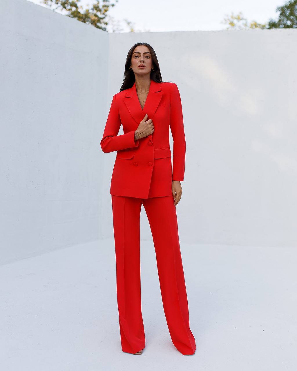 Woman wearing a red suit standing against a white wall.