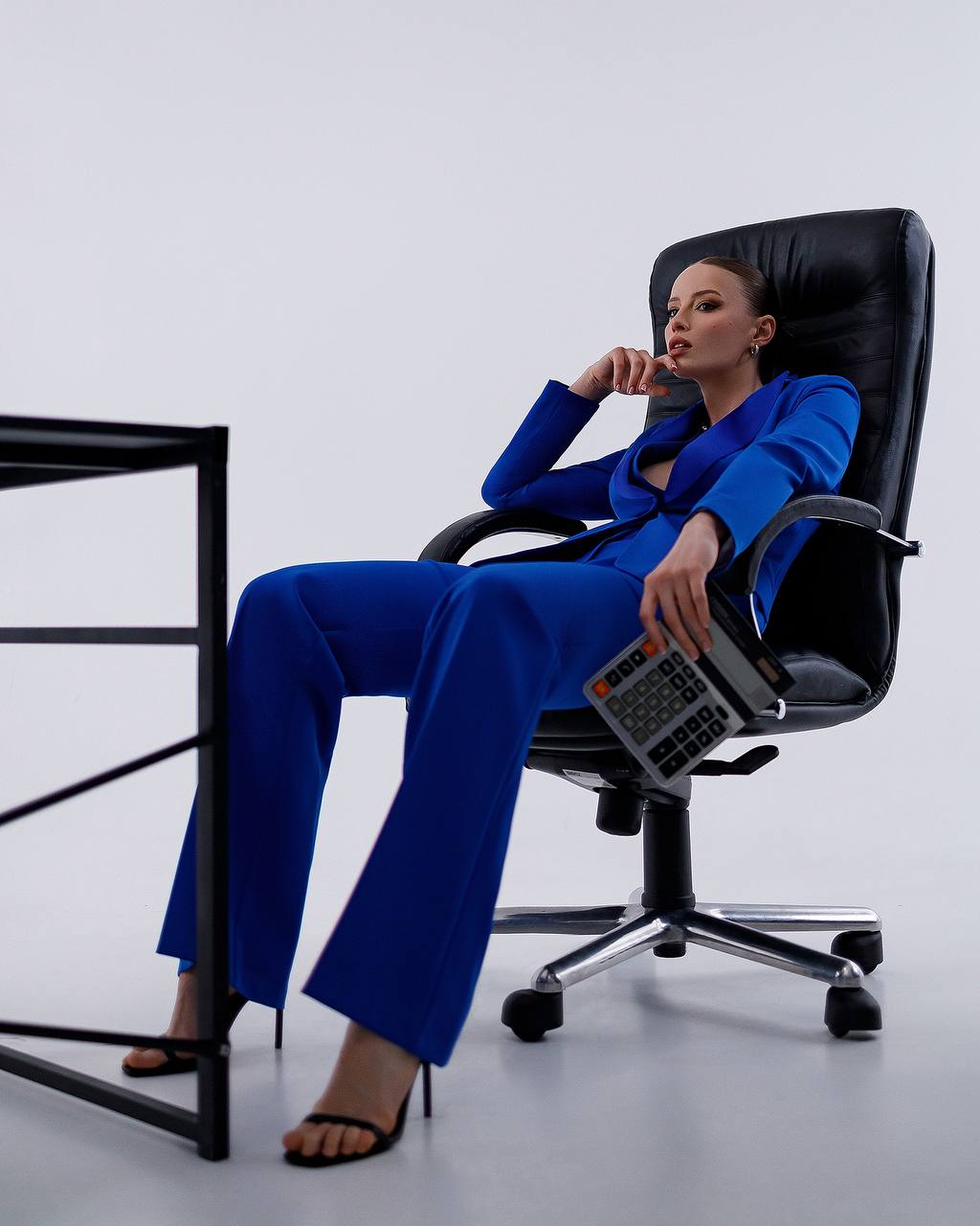 Woman in a blue suit sitting on a black office chair holding a phone.