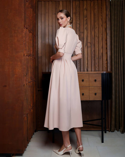 Woman in a beige dress standing in a room with wooden walls and furniture.