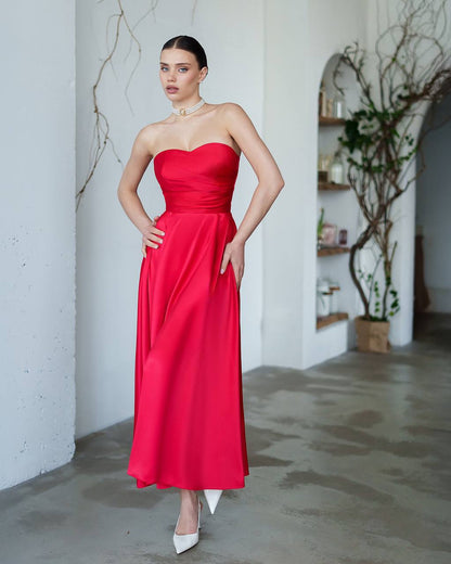 Woman wearing a red strapless dress in an indoor setting with white walls and minimal decor.