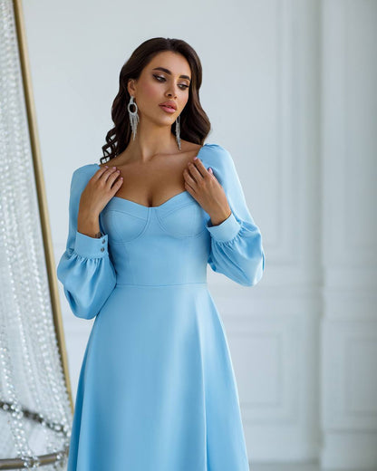 Woman wearing a light blue dress with long sleeves against a white background