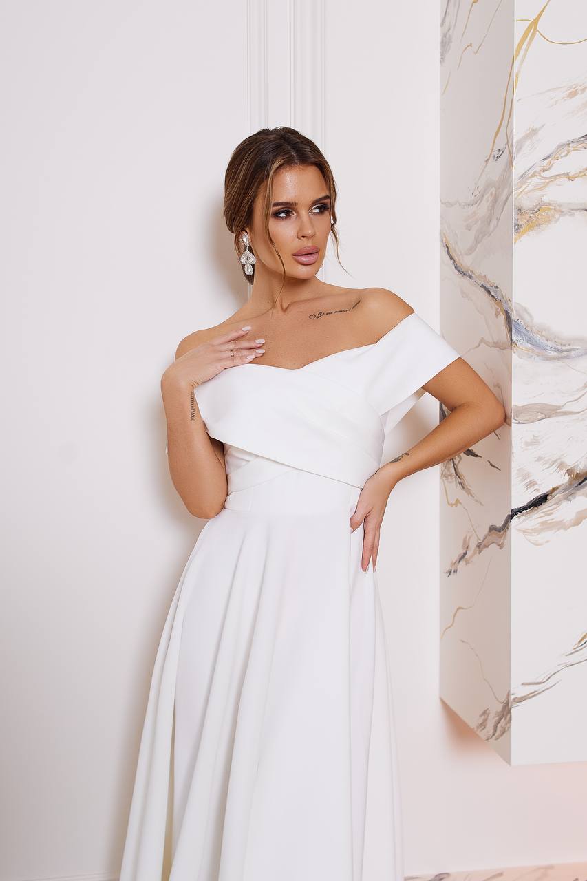 Woman wearing a white one-shoulder dress against a marble wall.