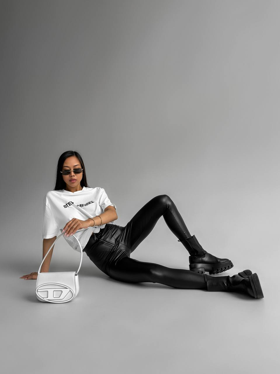 Person wearing a white t-shirt and black leather pants sitting on a gray background