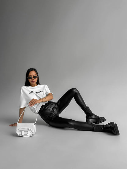 Person wearing a white t-shirt and black leather pants sitting on a gray background