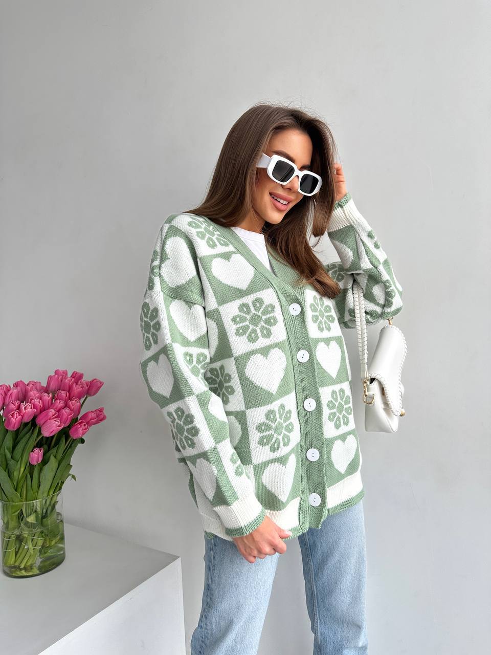 Woman wearing a green and white patterned cardigan with pink tulips in the background.