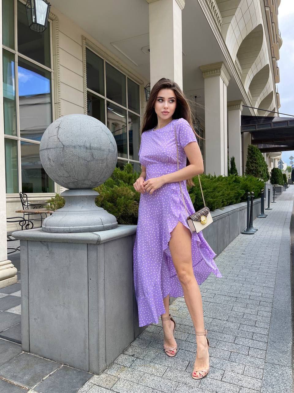 Woman in a purple dress standing on a sidewalk with a building in the background