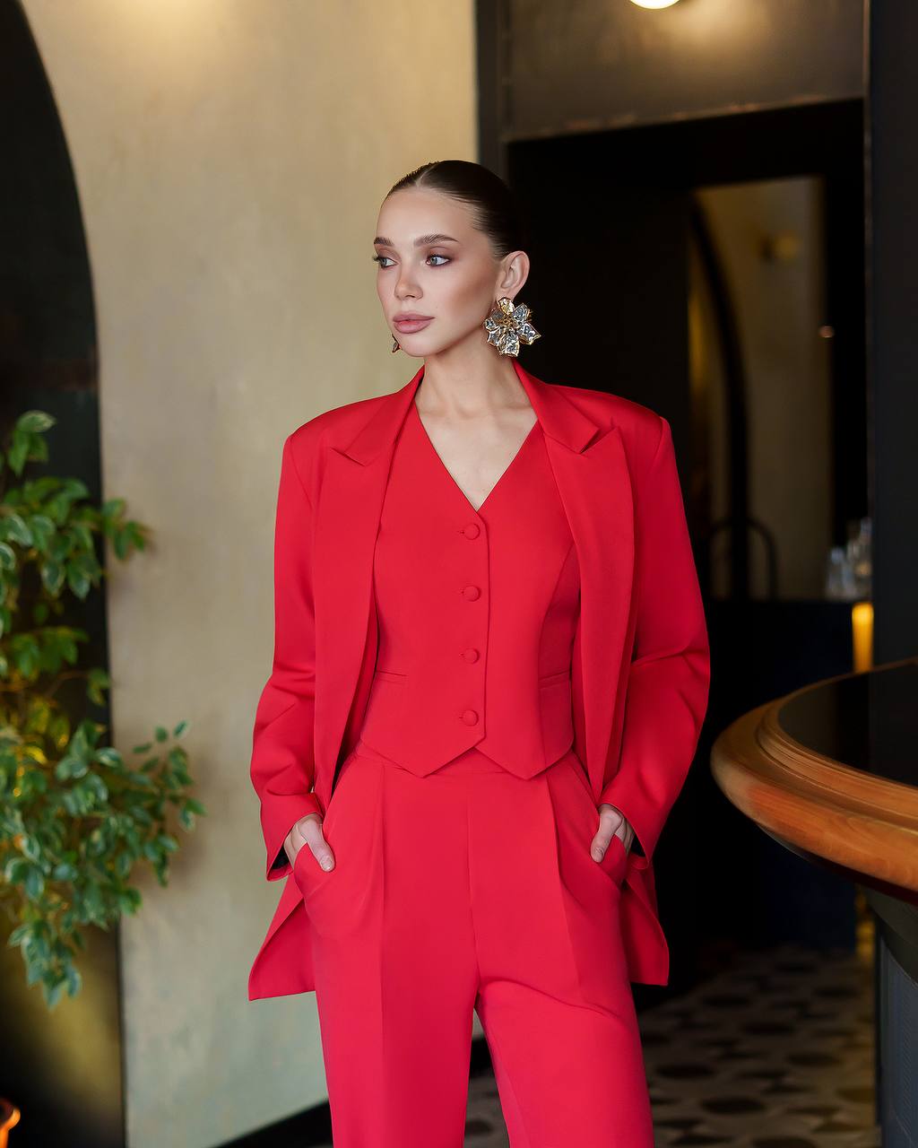 Woman in a red suit standing indoors with a blurred background