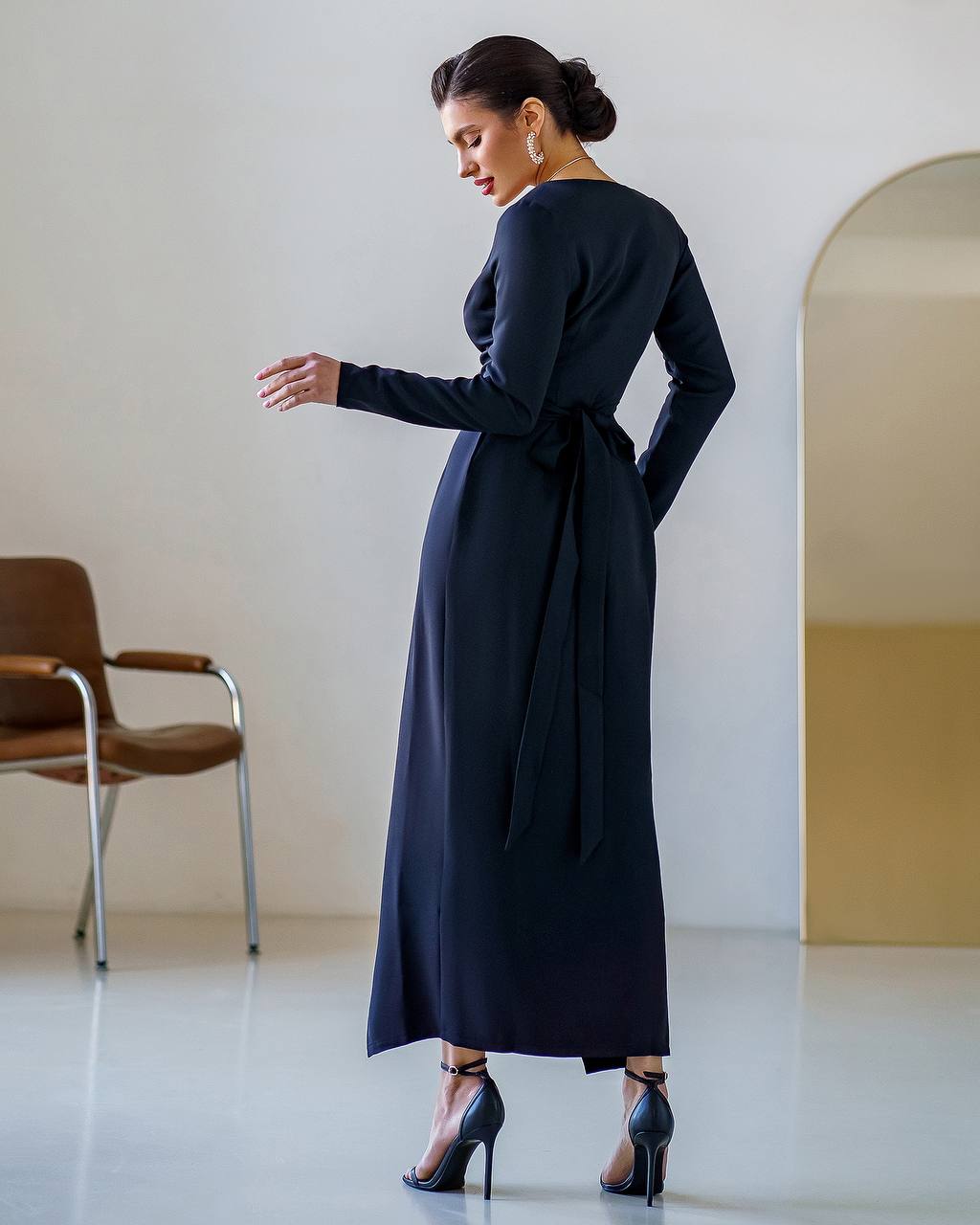 Woman wearing a long dark blue dress in a minimalistic room.