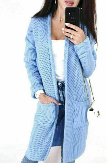 Person wearing a light blue cardigan with a white top and jeans, holding a phone.
