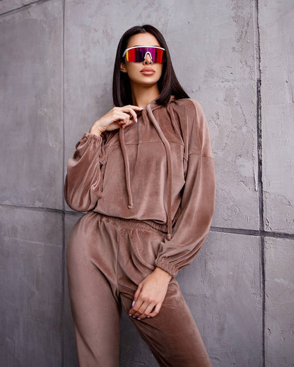 Person wearing a brown tracksuit with reflective sunglasses against a gray wall.